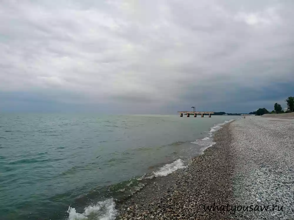 Вечений берег, вид на пирс. Вдалеке виднеется Гагра. Небольшие волны, тускнеющее небо и море сливающееся с горизонтом